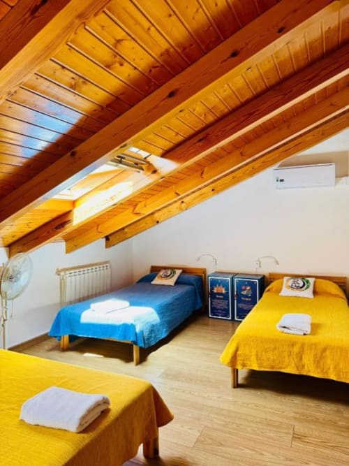 Dormitorio luminoso en la Albergue Só Por Hoje con tres camas, vigas de madera, claraboya y suelos de madera noble en Astorga.