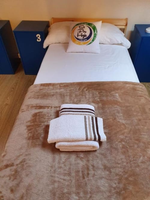 Cama individual impecable en habitación compartida del Albergue Só Por Hoje, Astorga, con almohadas blancas, toallas y manta beige