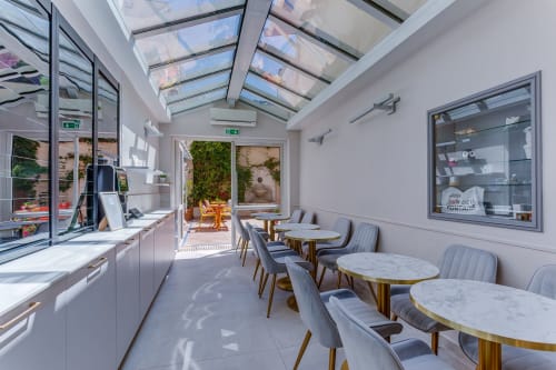 Modern hotel café at Hôtel De La Fontaine in Nice featuring skylights, marble tables, and garden views