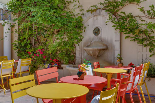 Colorful outdoor patio at Hôtel De La Fontaine in Nice with yellow and red chairs, round tables, climbing vines, and a wall