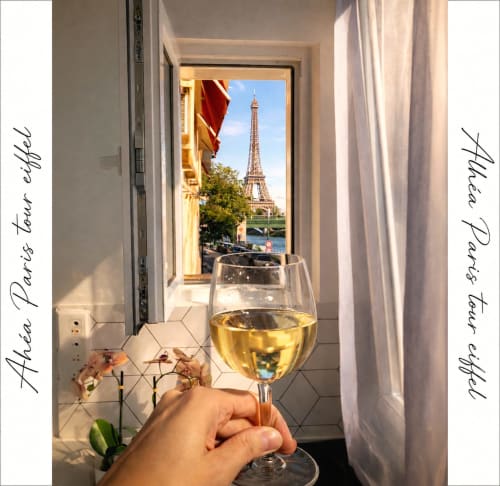 Main tenant un verre de vin blanc avec vue sur la Tour Eiffel depuis le balcon des Appartements ATHEA à Paris