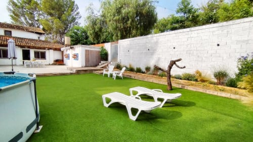Patio trasero de La Caseta de Ròtova con césped artificial, tumbonas blancas, piscina privada y terraza de paredes blancas