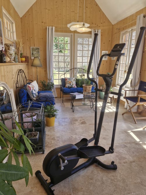 Home gym in wood-paneled sunroom at Casa Pertica B&B in Ceton, France with exercise bikes and seating.