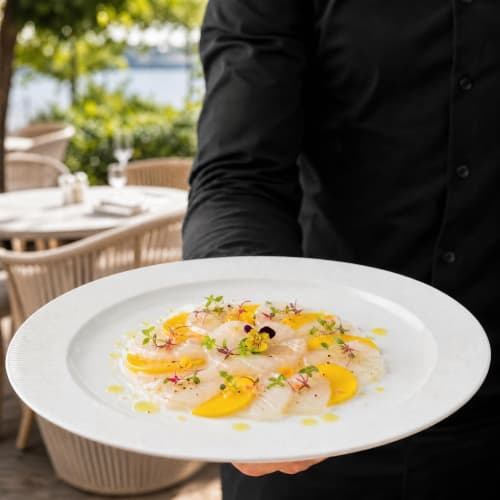 Chef présentant un élégant carpaccio de noix de Saint-Jacques aux agrumes et fleurs comestibles à Ô Château, Hayange