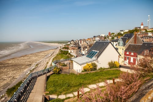Hidden Bay Hotel overlooks a picturesque French coastal town with beach, cliffs, and traditional architecture.