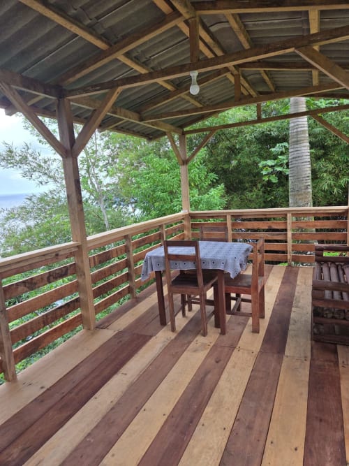 Varanda coberta em madeira com vista para o mar em Vila Paraíso, São Tomé. Área de refeições com mesa e cadeiras com vista para jardim tropical