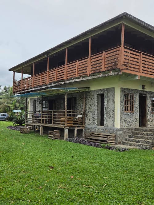 Casa Vila Paraíso em São Tomé com paredes de pedra e amarelas, varanda de madeira com vista ao jardim verdejante e ao mar
