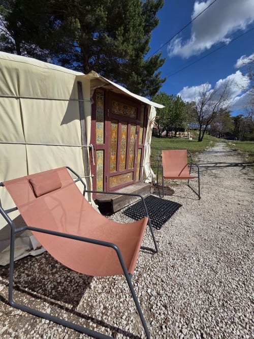 Cozy yurt exterior with terracotta lounge chairs at Destination Ailleurs, Castellane, featuring decorative red doors and