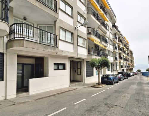 Edificio moderno de apartamentos en Sanxenxo con locales comerciales en planta baja, balcones y coches estacionados