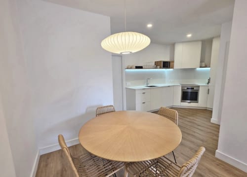Comedor moderno en Sanxenxo con mesa redonda de madera, lámpara colgante y cocina abierta en el hotel BR SILGAR