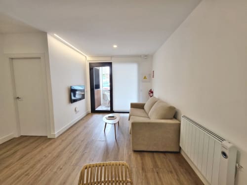Moderno salón en BR Silgar Sanxenxo con sofá beige, suelos de madera, TV y acceso a balcón