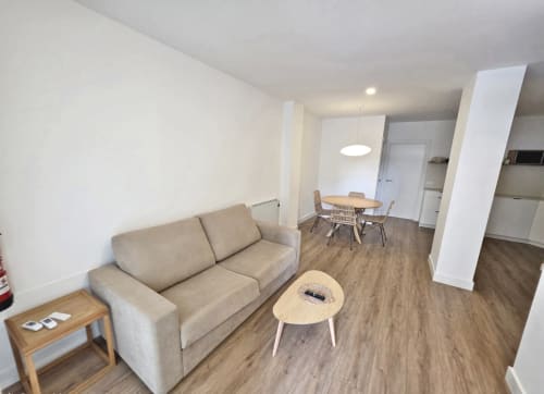 Moderno salón de apartamento en Sanxenxo con sofá beige, mesa de comedor y suelos de madera en BR SILGAR