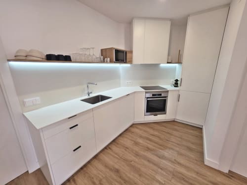 Cocina moderna blanca en apartamento BR Silgar, Sanxenxo. Distribución en L con horno empotrado, fregadero y piso de madera.