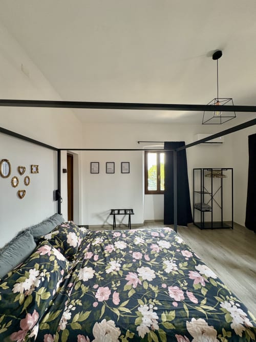 Camera da letto spaziosa a La Dolce Casa a Cremia con letto a baldacchino, biancheria floreale, travi nere e vista sul lago dalle finestre