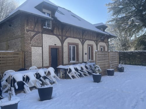 Snow-covered garden at Les Gites De Flaubert cottage in Le Héron, with lounge chairs and brick building