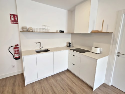 Cocina moderna en apartamento BR Silgar, Sanxenxo. Mobiliario blanco, fregadero de acero inoxidable, placa de cocción y estantería abierta.