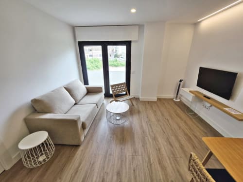 Moderna sala de estar del apartamento BR SILGAR en Sanxenxo con sofá beige, TV, suelo de madera y acceso a terraza
