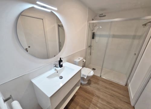 Baño moderno en BR SILGAR Sanxenxo con espejo redondo, lavamanos blanco, inodoro y ducha de acceso directo