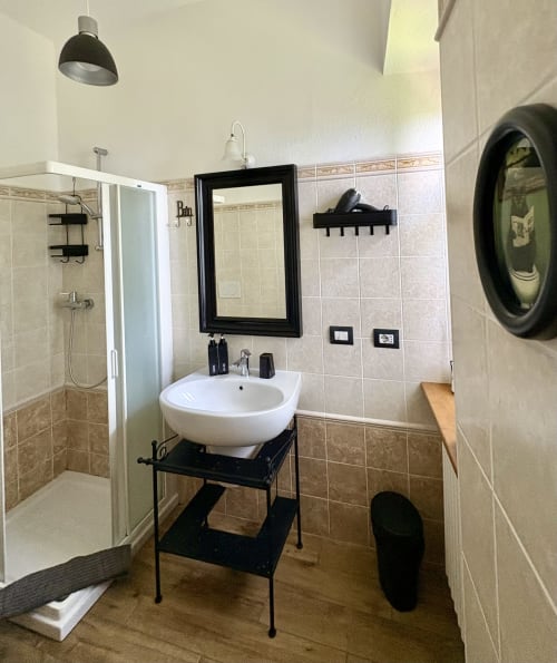 Bagno moderno con lavabo bianco a coppa, vanità nera e doccia a vista presso La Dolce Casa B&B a Cremia, Italia