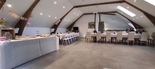 Elegant attic event space at Les Gites De Flaubert with vaulted beams, white linens, dining tables, and chandeliers.