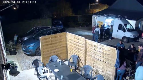 Night outdoor gathering at Les Gites De Flaubert villa with wooden fence, dining table, and guests near white van