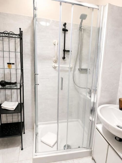 Modern glass shower enclosure with black fixtures in Vatican Living Rome bathroom, featuring white tile walls and rainfall