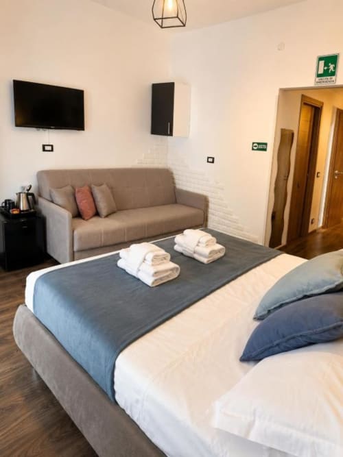Modern bedroom at Vatican Living Rome with bed, grey sofa, wall-mounted TV, and hardwood floors