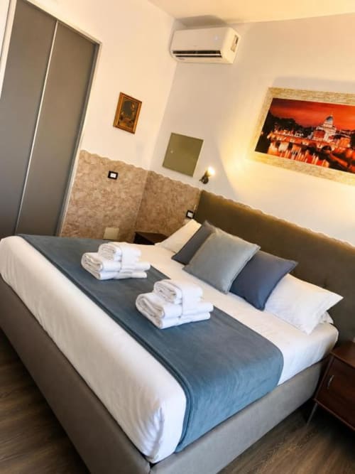 Modern hotel bedroom at Vatican Living Rome with double bed, white towels, blue accent pillows, air conditioning unit, and