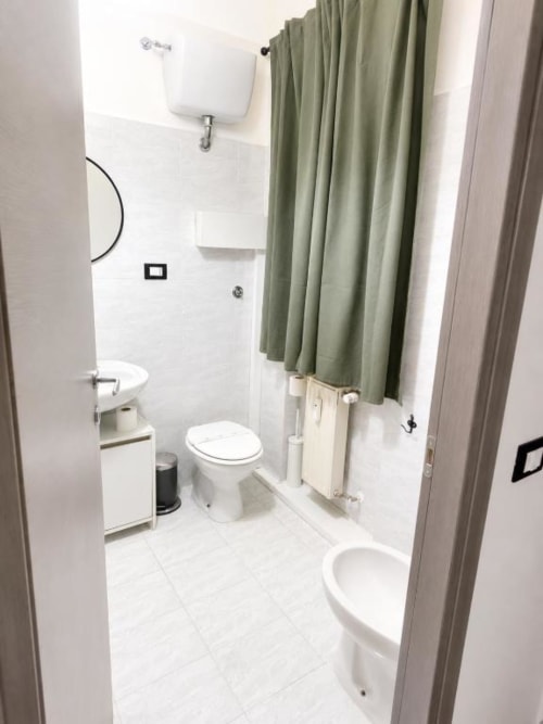 Clean modern bathroom with white tile, toilet, sink, and sage green shower curtain at Vatican Living Rome hotel in Rome