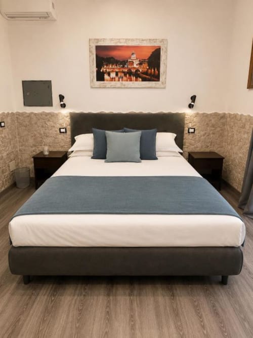 Modern bedroom at Vatican Living Rome B&B with dark headboard, white bedding, blue pillows, and framed city view art above