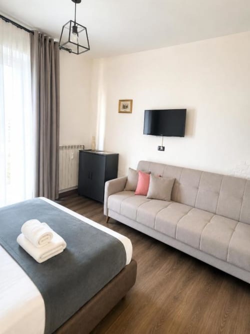 Modern bedroom at Vatican Living Rome with bed, beige sofa, flat-screen TV, and garden view