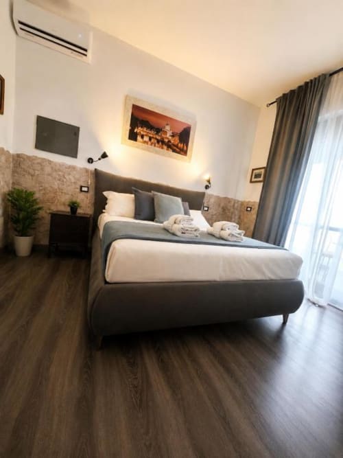 Modern double bedroom at Vatican Living Rome with dark bed, beige walls, wooden floors, AC unit, wall-mounted TV, and glass