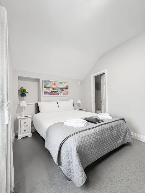 Modern bedroom at Madeline's Accommodation in Wicklow with queen bed, white bedding, and coastal artwork