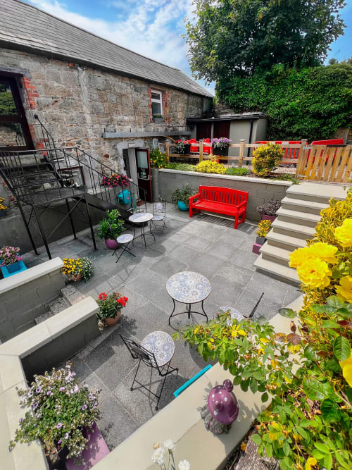 Madeline's Accommodation courtyard in Wicklow featuring red benches, flowering plants, and seating areas