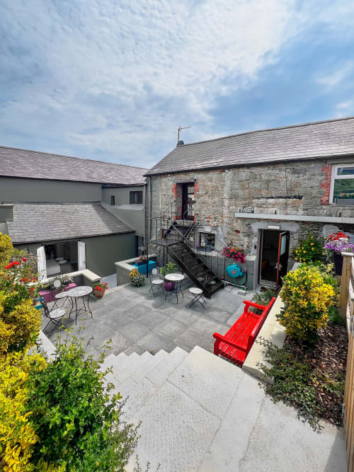 Madeline's Accommodation courtyard in Wicklow with stone buildings, dining tables, flowers, and red bench under blue sky