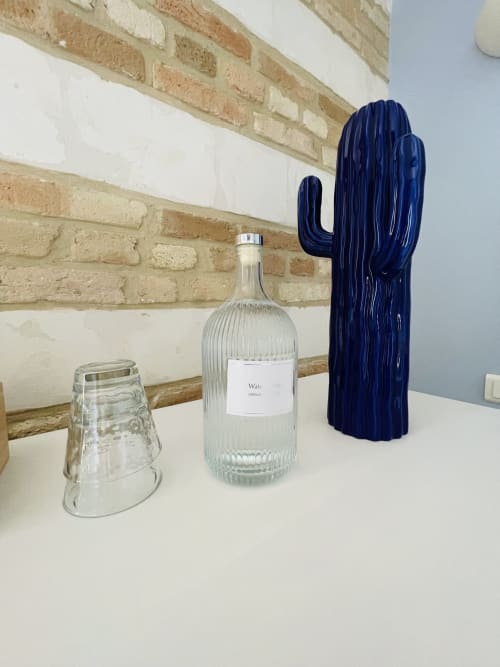 Étagère stylisée à Maison Nolette avec sculpture de cactus bleu, bouteille en verre et verrerie texturée contre mur en brique