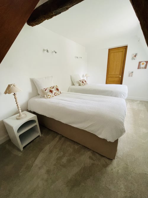 Chambre lumineuse à la Maison Nolette avec lits jumeaux, draps blancs, plafond à poutres et porte en bois à Noyelles sur Mer