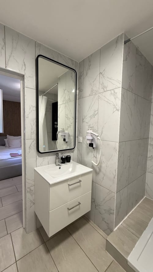 Salle de bains moderne à la Kimi Résidence, Cannes avec carrelage marbre, vasque blanche et miroir encadré