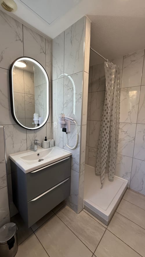 Salle de bains moderne à Kimi Résidence Cannes avec carrelage marbre, vasque élégante, miroir rétroéclairé et douche à l'italienne.