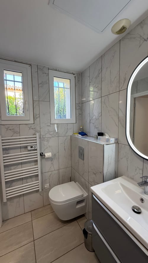 Salle de bains moderne en marbre à la Résidence Kimi Cannes avec toilettes murales, lavabo, sèche-serviettes chauffant et miroir lumineux