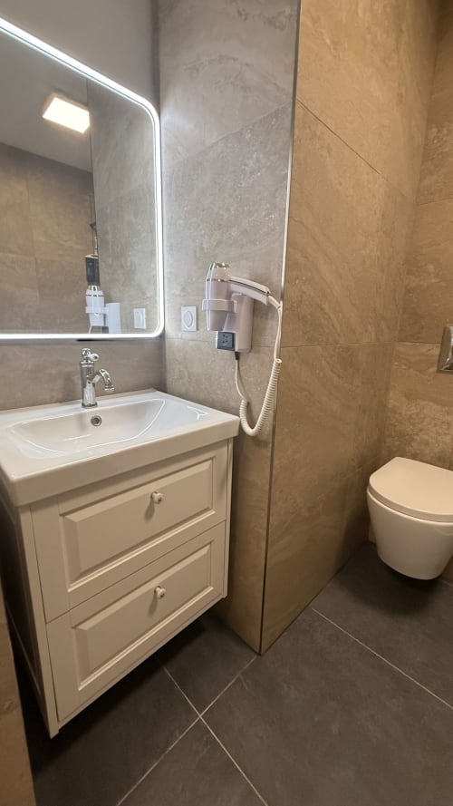 Salle de bain moderne de la Chambre Deluxe Kimi Résidence, Cannes : vasque blanche, miroir lumineux, carrelage, toilettes et douche