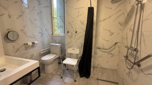 Salle de bains moderne du studio Kimi Résidence à Cannes, avec carrelage marbre, toilettes, lavabo, douche avec rideau noir