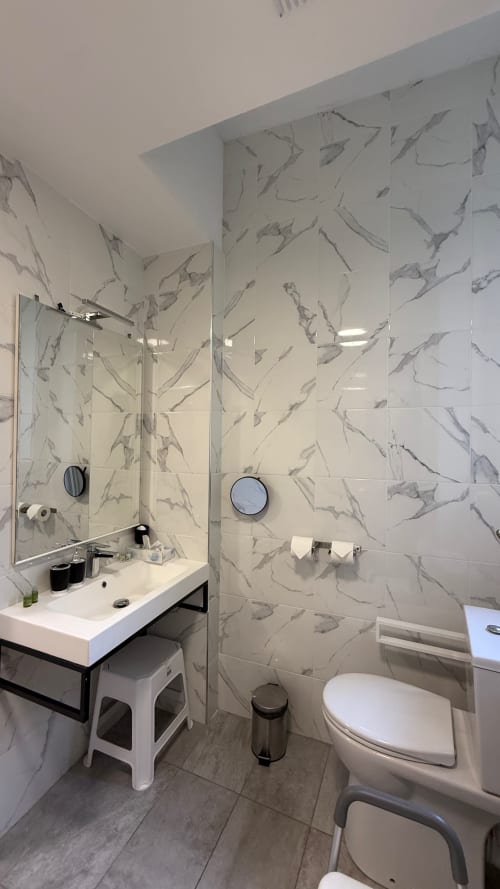 Salle de bain moderne à Kimi Résidence à Cannes avec carrelage imitation marbre, lavabo blanc, douche vitrée et toilettes