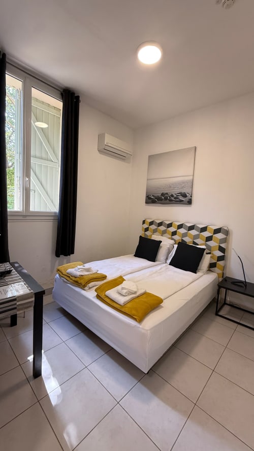 Chambre moderne à Kimi Résidence Cannes avec lit blanc, tête de lit géométrique et vue sur le jardin