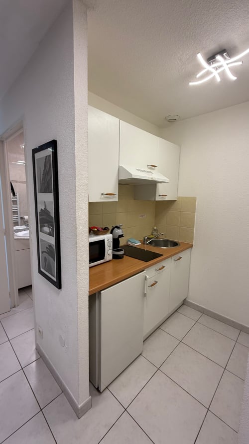 Kitchenette compacte du studio Kimi Résidence à Cannes : armoires blanches, plan de travail en bois, cuisinière, évier et électroménagers