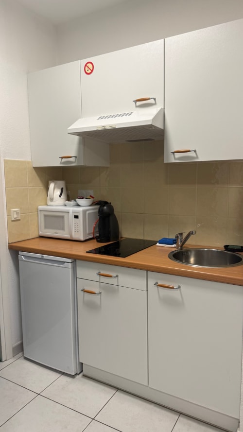 Kitchenette de studio à la Kimi Résidence Cannes avec armoires blanches, plan de travail en bois, micro-ondes et plaque de cuisson à induction