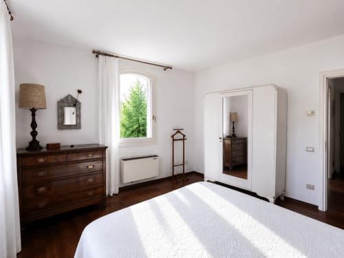 Camera luminosa a Palazzo Bonfiglioli con letto in legno, cassettone antico, armadio e vista giardino dalla finestra ad arco