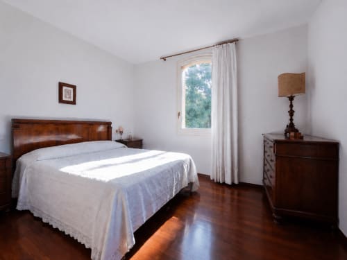 Camera luminosa a Palazzo Bonfiglioli con letto in legno, biancheria bianca, cassettiera in legno scuro e finestra con vista sul giardino