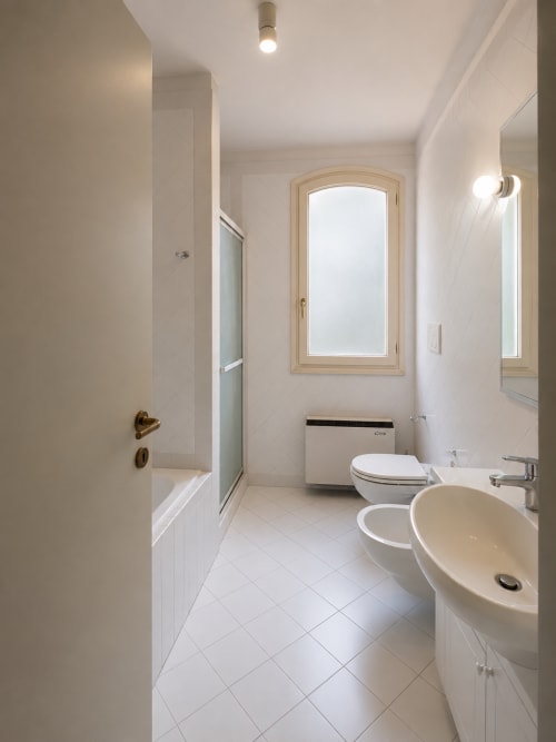 Bagno moderno a Palazzo Bonfiglioli con lavabo color crema, wc, doccia e finestra ad arco con vista sul giardino