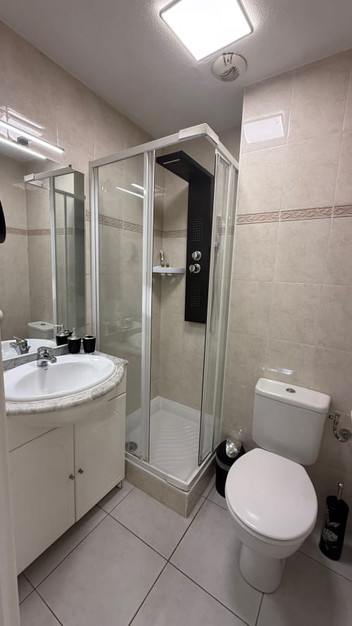 Salle de bains moderne à la Kimi Résidence de Cannes avec douche, lavabo blanc, toilettes et carrelage beige
